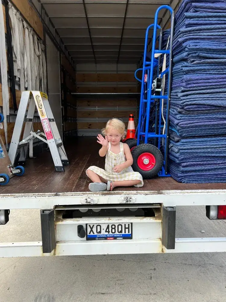 A child sitting beside blankets and trolleys inside the family moving truck