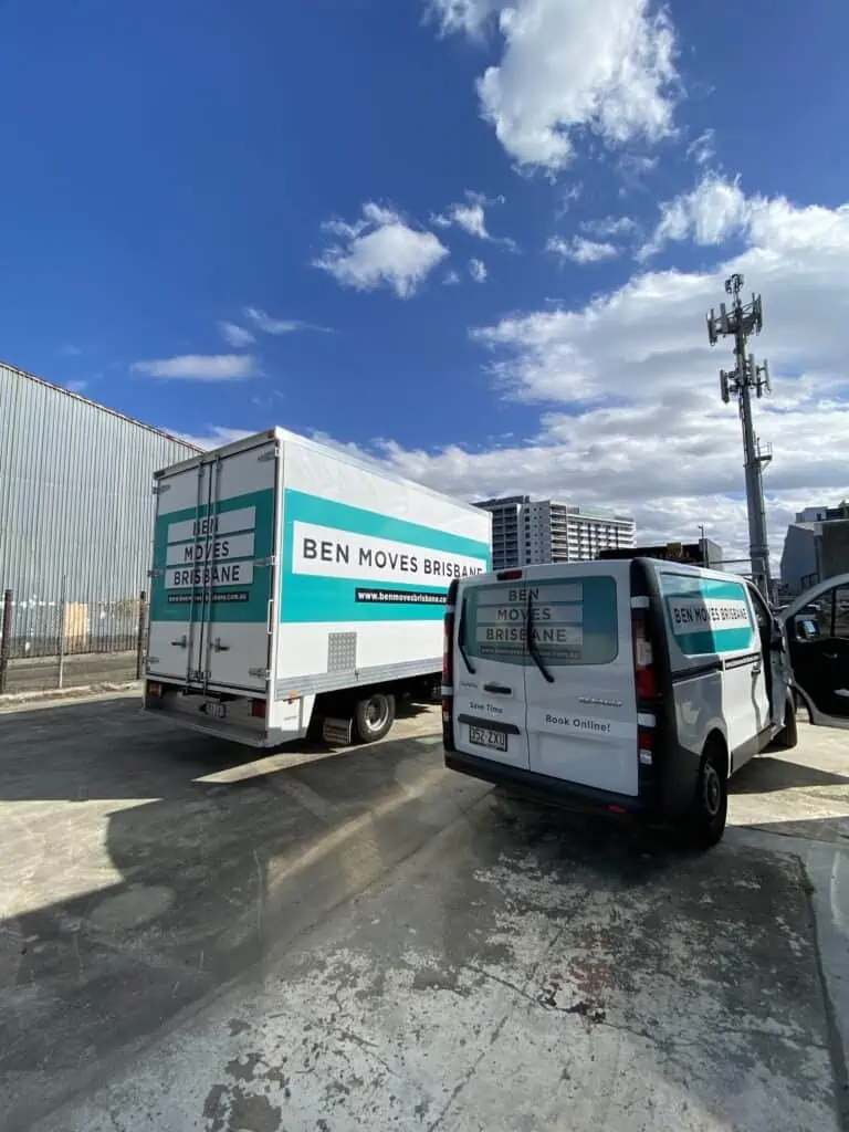 A moving van and moving truck parked on concrete with blue cloudy sky in the background