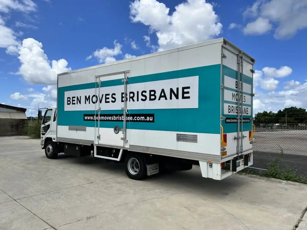 A moving truck parked on concrete in front of a wire fence